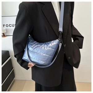 Detail of light blue quilted crossbody bag with metallic finish and wide fabric strap