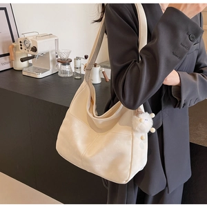 Detail view of off-white hobo bag with plush charm in a minimalist cafe setting