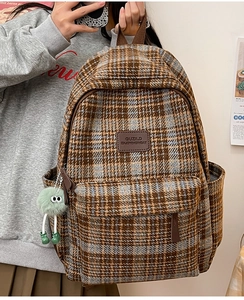 Détail d'un sac à dos à carreaux marron avec charm vert et écusson de logo en cuir