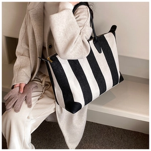 Dettaglio della borsa tote in tela a righe con finiture in pelle nera indossata da modella