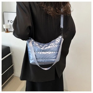 Modern quilted down crossbody bag in metallic blue worn by model in minimalist setting
