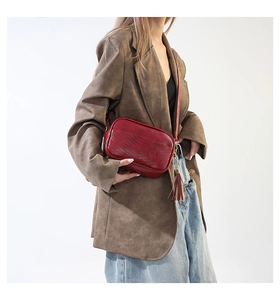 Detailed view of deep red crossbody bag with tassel on a model wearing a brown blazer
