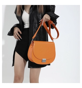 Gros plan d'un sac selle orange avec bandoulière large et fermoir métallique argenté