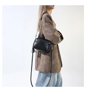 Detail of a chic black faux leather crossbody bag featuring stylish side tassel decor