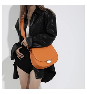 Détail du sac besace orange vif avec boucle argentée porté sur une veste en cuir