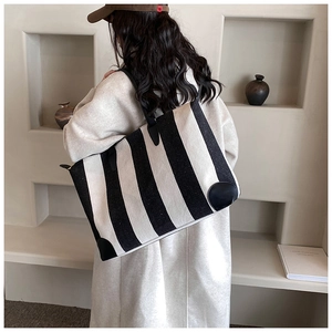 Modella che indossa una borsa tote a righe con cinturini in pelle su sfondo minimalista