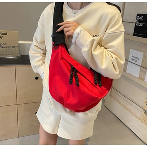 Detail of red crescent crossbody bag featuring wide black strap and rope zipper pull