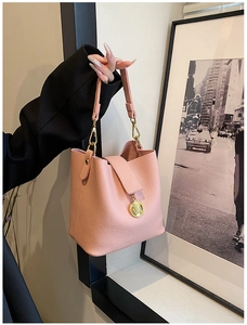 Gros plan sur le sac seau rose en similicuir avec détails dorés et pendentif logo