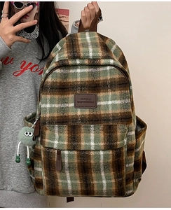 Détail du sac à dos en peluche à carreaux avec logo en cuir marron et pompon vert décoratif