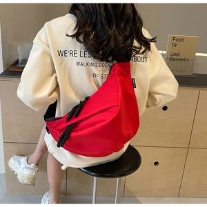 Detail view of a large red nylon crescent crossbody bag worn on a beige sweatshirt