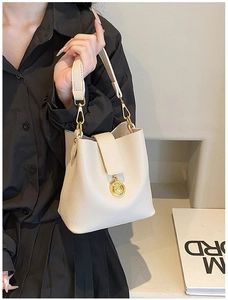 Détail du sac seau blanc cassé avec motif litchi, finitions dorées et pendentif relief