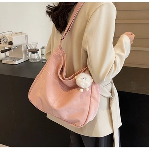 Detailed side view of pink faux suede shoulder bag with plush pendant on a model
