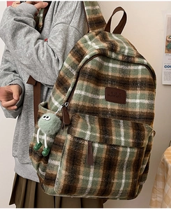 Détail d'un sac à dos écossais vintage avec logo en cuir marron et charm en peluche
