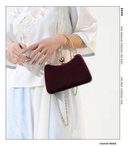 Deep burgundy velvet handbag with gold chain strap shown in elegant lifestyle scene