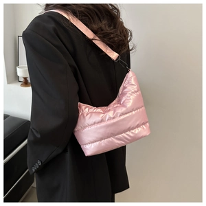 Pink quilted puffer bag made of satin fabric with metallic shine on female model shoulder