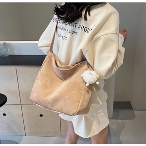 Detail of a large apricot suede tote bag featuring a cute white plush ball pendant