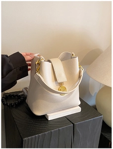Détail du sac seau crème montrant la texture du cuir grainé et le médaillon doré