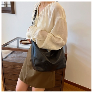 Close-up of stylish black glossy PU leather hobo bag with sleek minimalist shoulder strap
