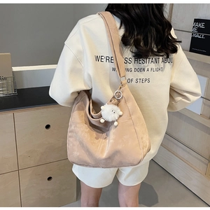 Detail of a large apricot suede shoulder bag with a cute plush monster charm on a model