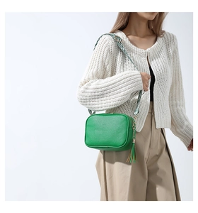 Detail of green leather crossbody bag with ethnic tassels and woven shoulder strap