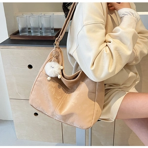 Detail of beige suede tote bag with plush ball charm shown in a cozy indoor lifestyle setting
