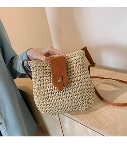 Close-up of woven raffia crossbody bag with brown leather strap and metal buckle closure