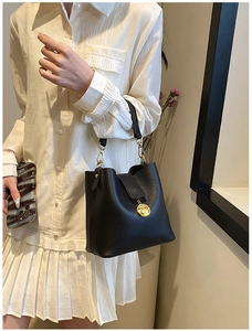 Détail d'un sac seau noir chic en cuir texturé avec un médaillon doré élégant