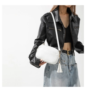 Detail view of a white pebbled faux leather crossbody bag with long fringe tassel on model