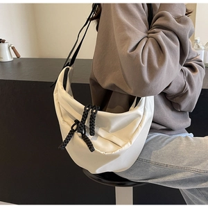 Detail of white crescent crossbody bag showing black woven rope zipper pull and canvas texture