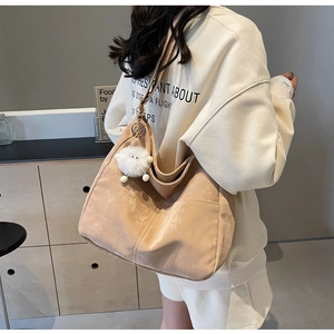 Detail view of khaki faux suede tote bag with a white plush pompom charm and shoulder strap
