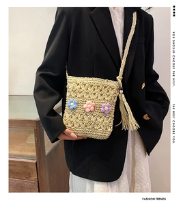 Detail of straw crossbody bag with crochet flowers and tassel shown on a model