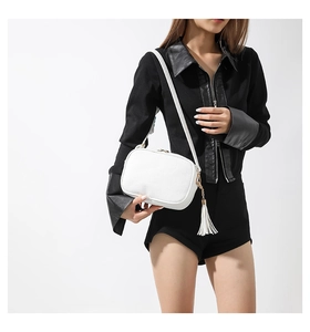 Close-up of white pebble leather crossbody bag with golden zipper and fringe tassel