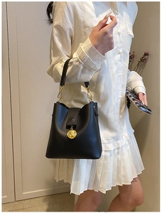 Détail du sac seau en cuir grainé noir avec pendentif pièce dorée sur robe