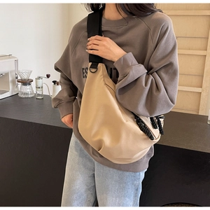 Detail of a beige nylon crescent crossbody bag with a wide black strap and woven puller
