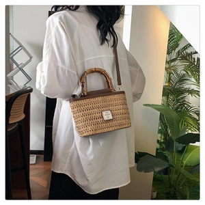 Close-up of woven straw handbag featuring bamboo handle and leather strap detail