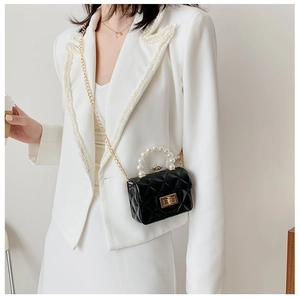 Détail du mini sac noir avec poignée en perles et chaîne dorée porté par le mannequin