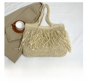 Dettaglio di una borsa tote in paglia beige con lunghe frange e trama in corda di carta