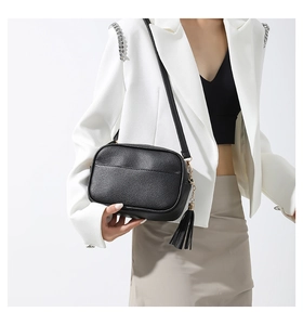 Detail of black pebbled leather crossbody bag with tassel and adjustable shoulder strap