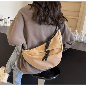 Rear view of khaki half-moon canvas crossbody bag worn by a model in a cozy cafe