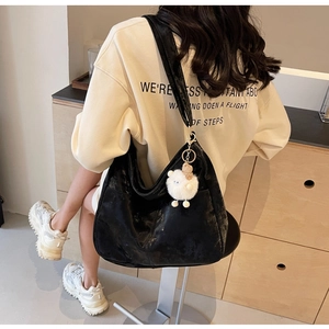 Macro detail of black hobo shoulder bag with a cute white plush lamb keychain charm