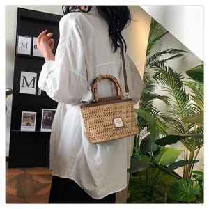 Detail of woven straw bag with natural bamboo handle and brown leather shoulder strap