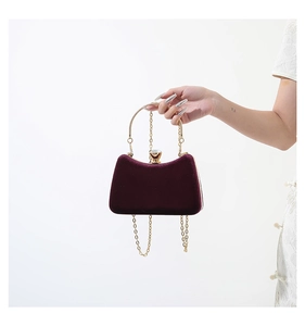 Detail of burgundy velvet evening bag featuring crystal clasp and gold circular handle