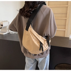 Close-up of beige half-moon crossbody bag with black adjustable strap worn by model