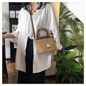 Close-up of woven straw handbag featuring a natural bamboo handle and brown leather strap