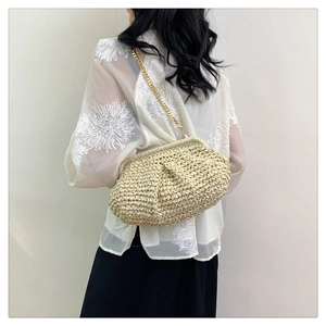 Detail of beige woven straw clutch bag featuring a golden chain strap and pleated silhouette