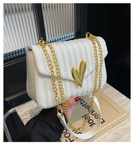 Detail of white quilted handbag featuring a golden heart-shaped clasp and chain strap