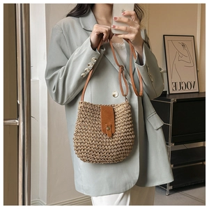 Detailed close-up of woven raffia shoulder bag with brown leather strap and gold clasp