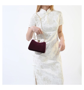 Close-up of burgundy velvet evening clutch with gold handle and stone-shaped metal clasp