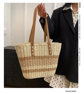 Detail of woven straw tote bag with brown stripes and leather handles shown by model