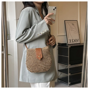 Detail of a straw woven crossbody bag with brown leather flap and stylish metal buckle